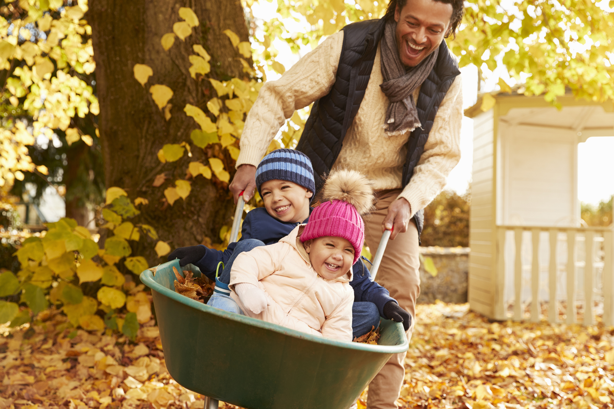 Father with children in wheelbarrow playing in the fall leaves