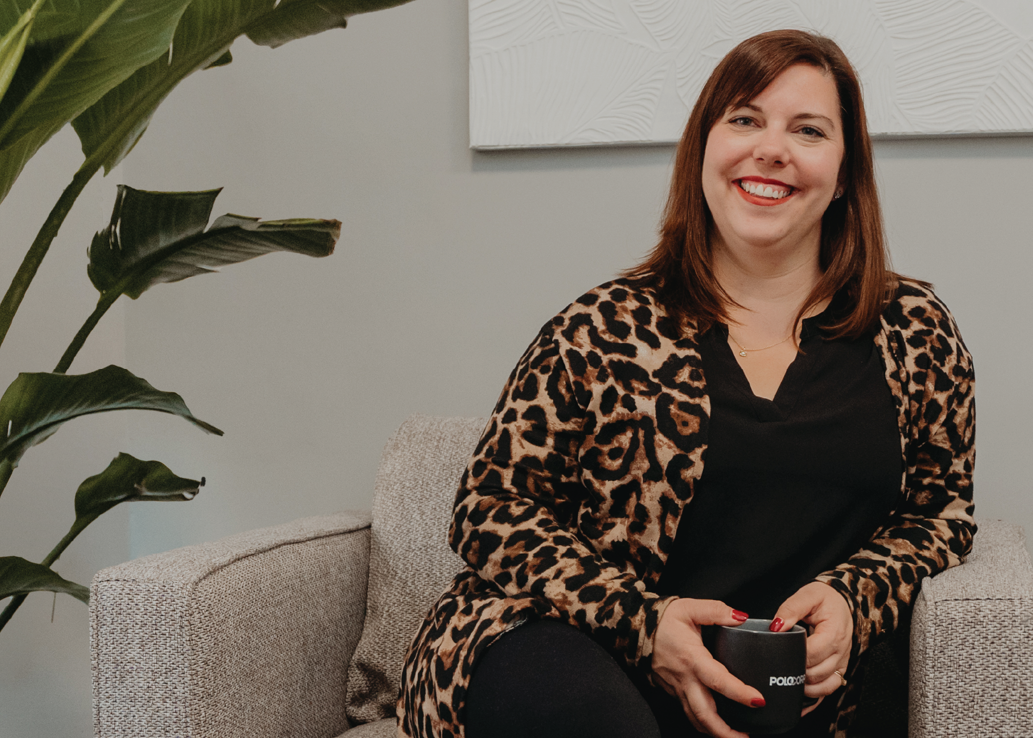 Nicole, sitting on a couch with coffee smiling